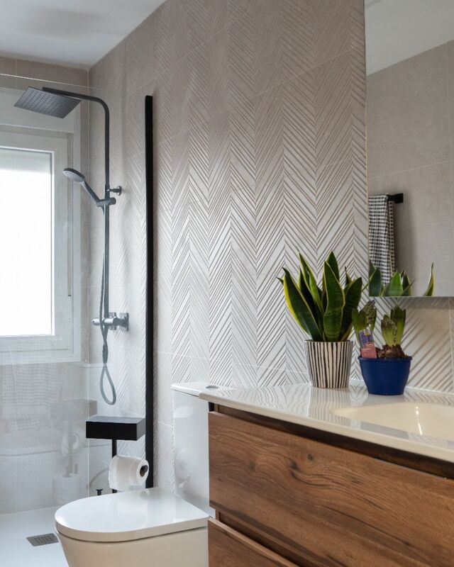 Baño reformado con revestimiento en relieve de espiga, ducha con columna negra mate y mueble de lavabo con acabado roble
