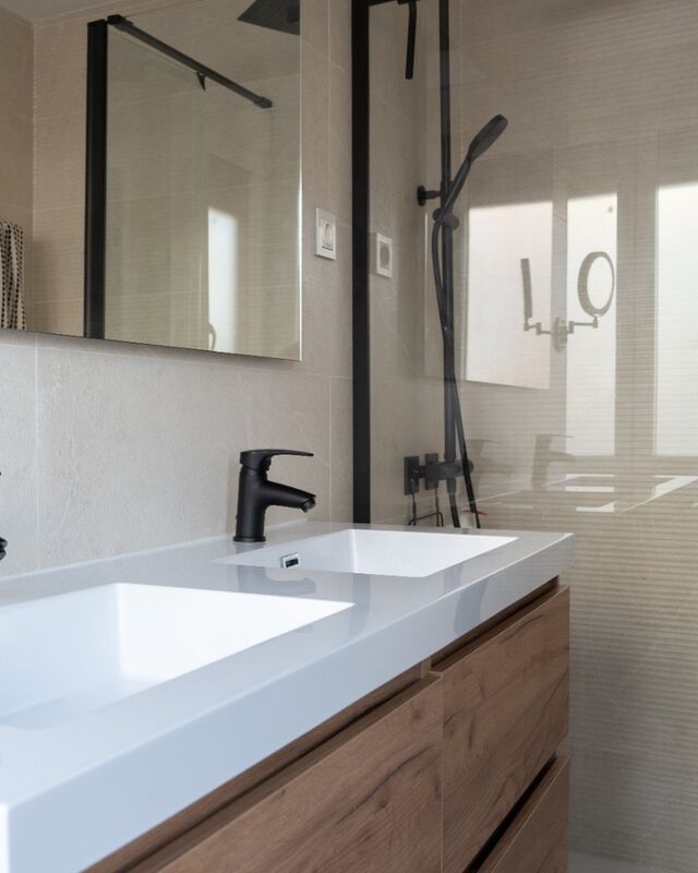Mueble de lavabo junto a la ducha con mampara de vidrio y perfil negro
