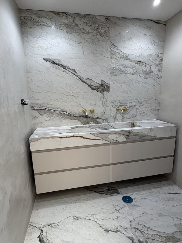 Baño revestido con porcelánico de gran formato efecto mármol, lavabo integrado y grifería empotrada en oro cepillado