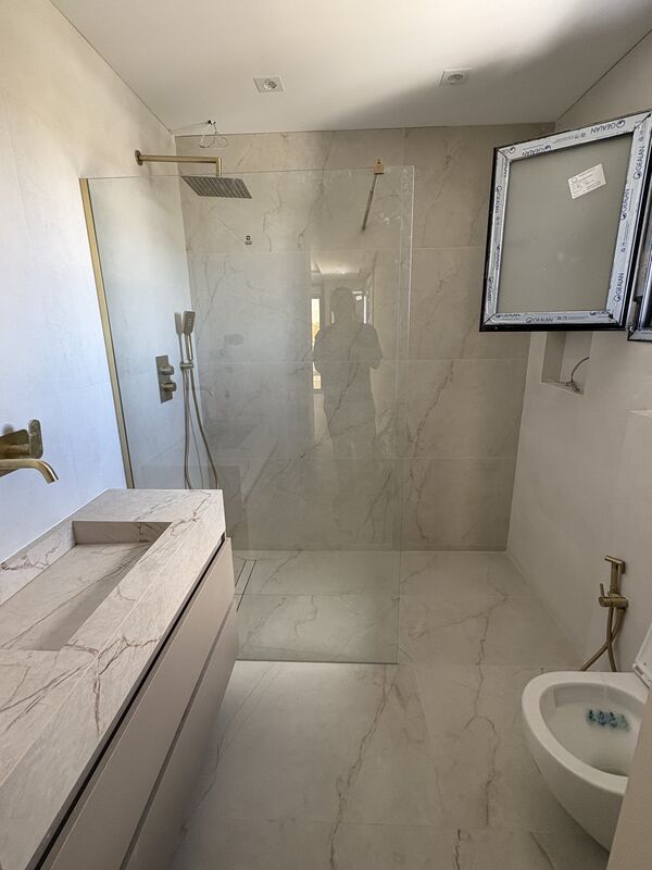 Segundo baño con ducha a ras de suelo, mampara fija y grifería en oro cepillado
