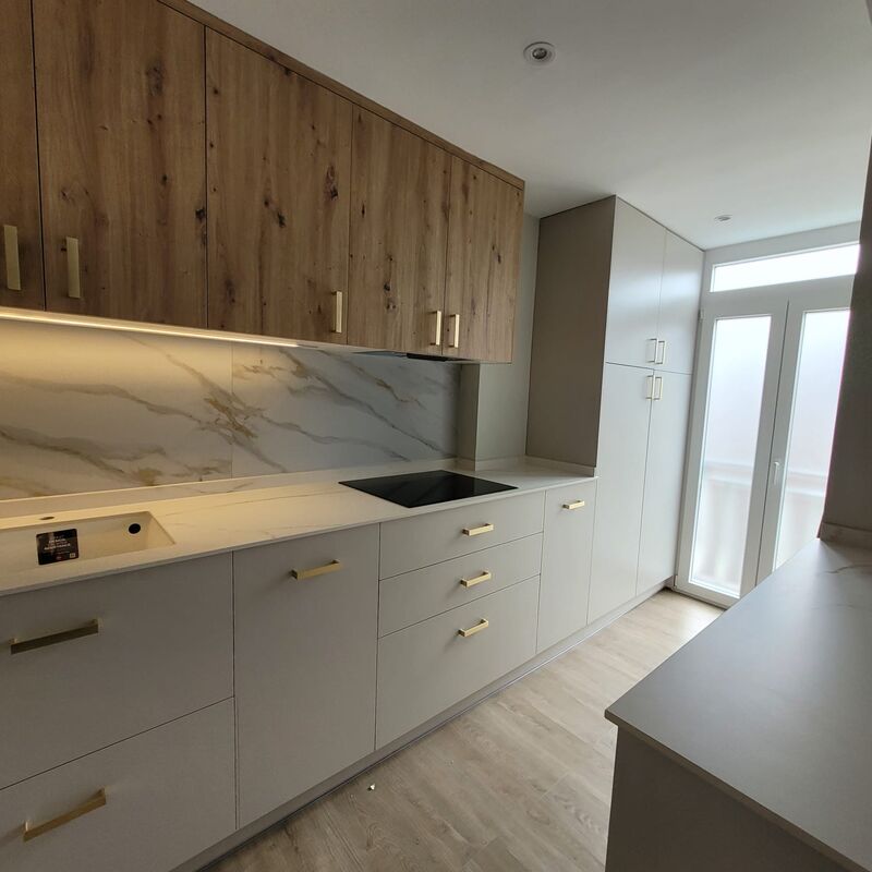 Cocina reformada con muebles altos en acabado roble, frontal de porcelánico efecto mármol y tiradores de latón