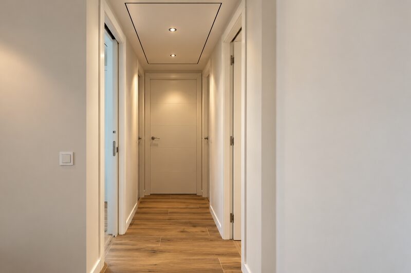Pasillo con puertas lacadas en blanco, suelo de madera y techo con foseado e iluminación empotrada